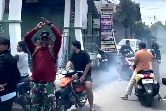 
					Seorang anggota TNI dari Koramil Wonodadi memberi isyarat tangan kepada pengunjuk rasa yang menggeber mesin sepeda motor di depan Kantor Desa Wonodadi, Kecamatan Wonodadi, Kabupaten Blitar, Selasa (13/1/2026) (Dok. Warga Wonodadi)